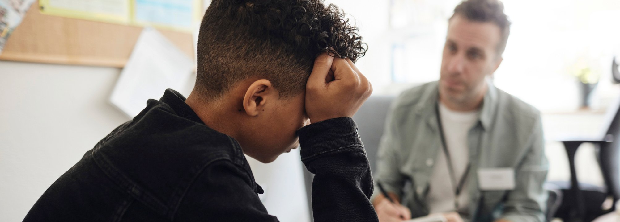 Nedstämd tonårspojke samtalar med vuxen skolpersonal.